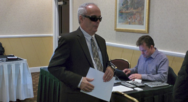 A senior man reads a Braille page in the exhibit hall.